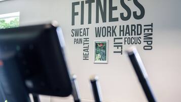 A gym wall with motivational words like FITNESS, SWEAT, PAIN, HEALTH, WORK HARD, TEMPO, and LIFT.