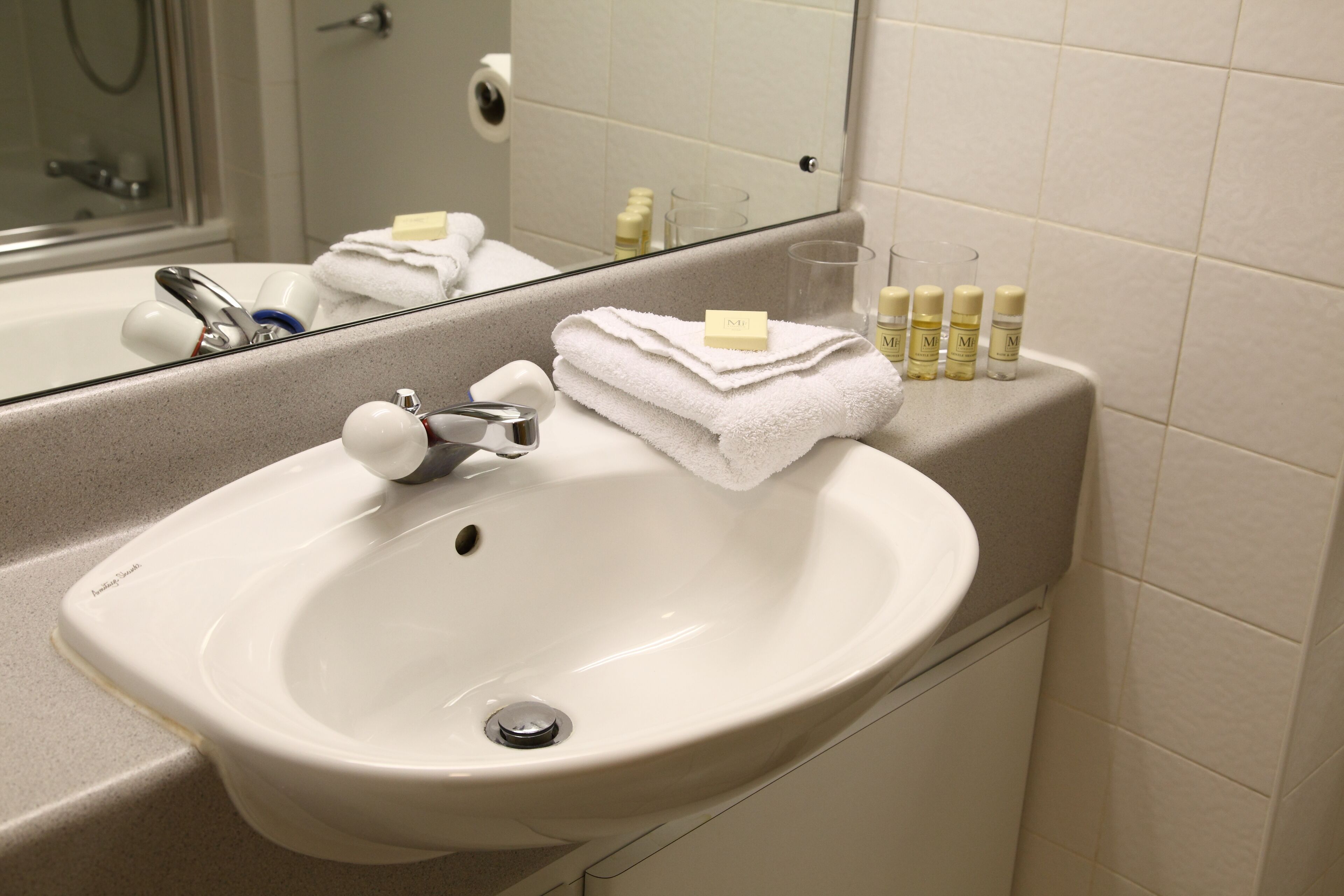 Une salle de bain avec un lavabo blanc, un miroir et des articles de toilette posés sur le comptoir.