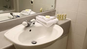 Une salle de bain avec un lavabo blanc, un miroir et des articles de toilette posés sur le comptoir.