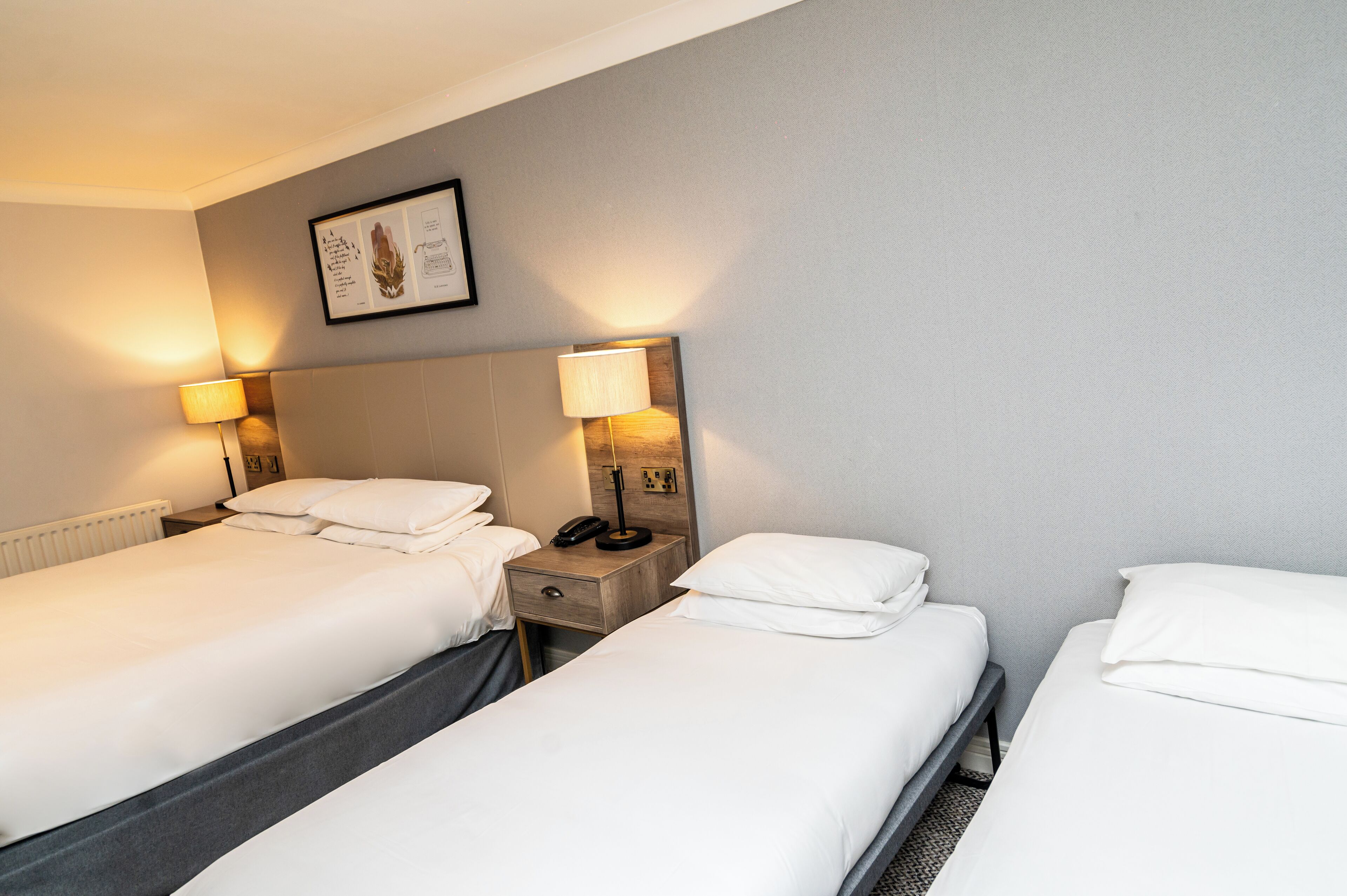 A hotel room with two single beds, bedside tables with lamps, a framed picture on the wall, and a radiator under the beds.