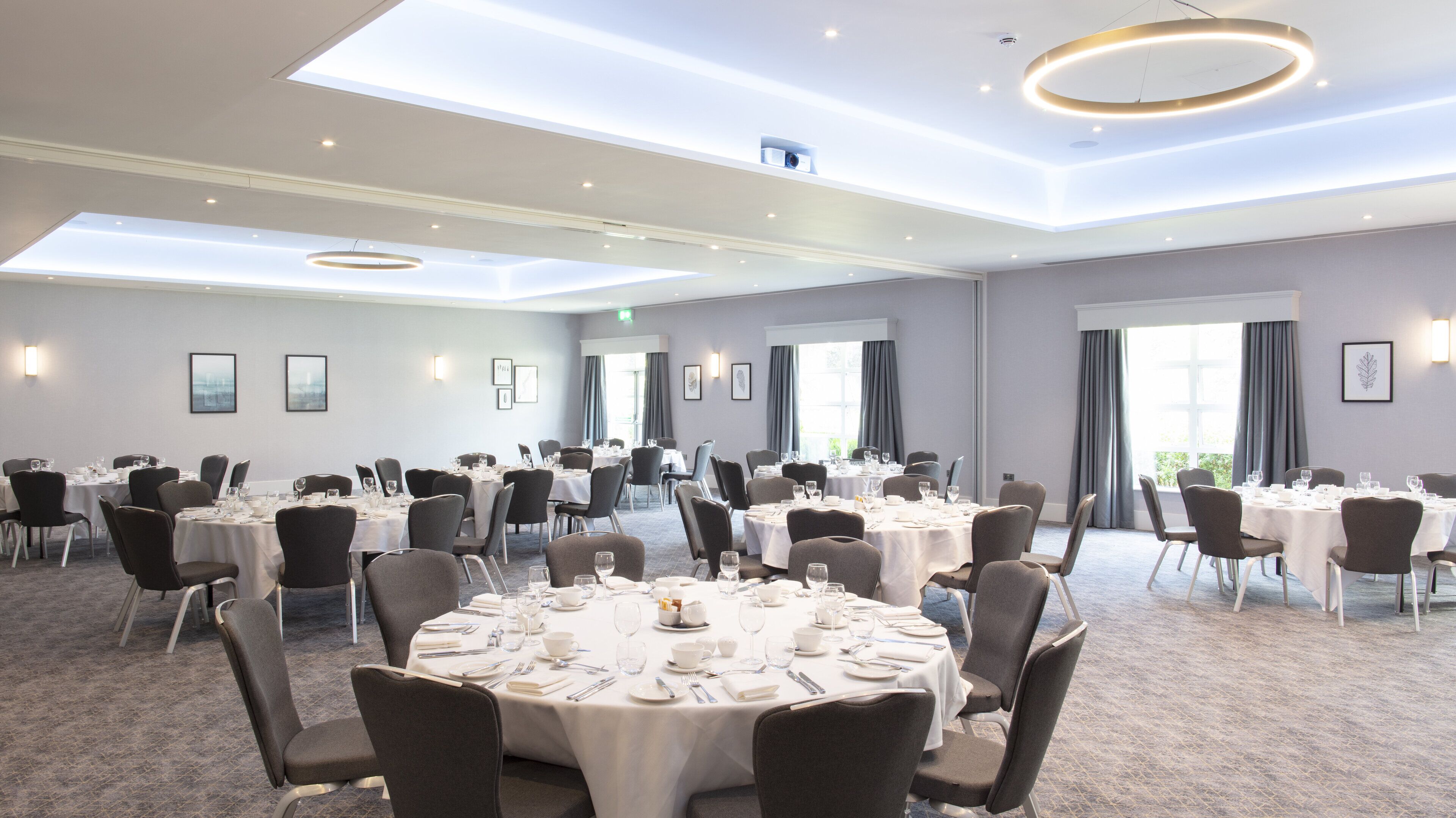 A large conference room with multiple round tables, each set with white tablecloths, chairs, and dining essentials.