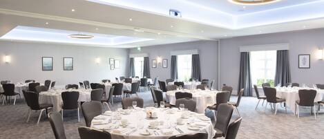 A large conference room with multiple round tables, each set with white tablecloths, chairs, and dining essentials.