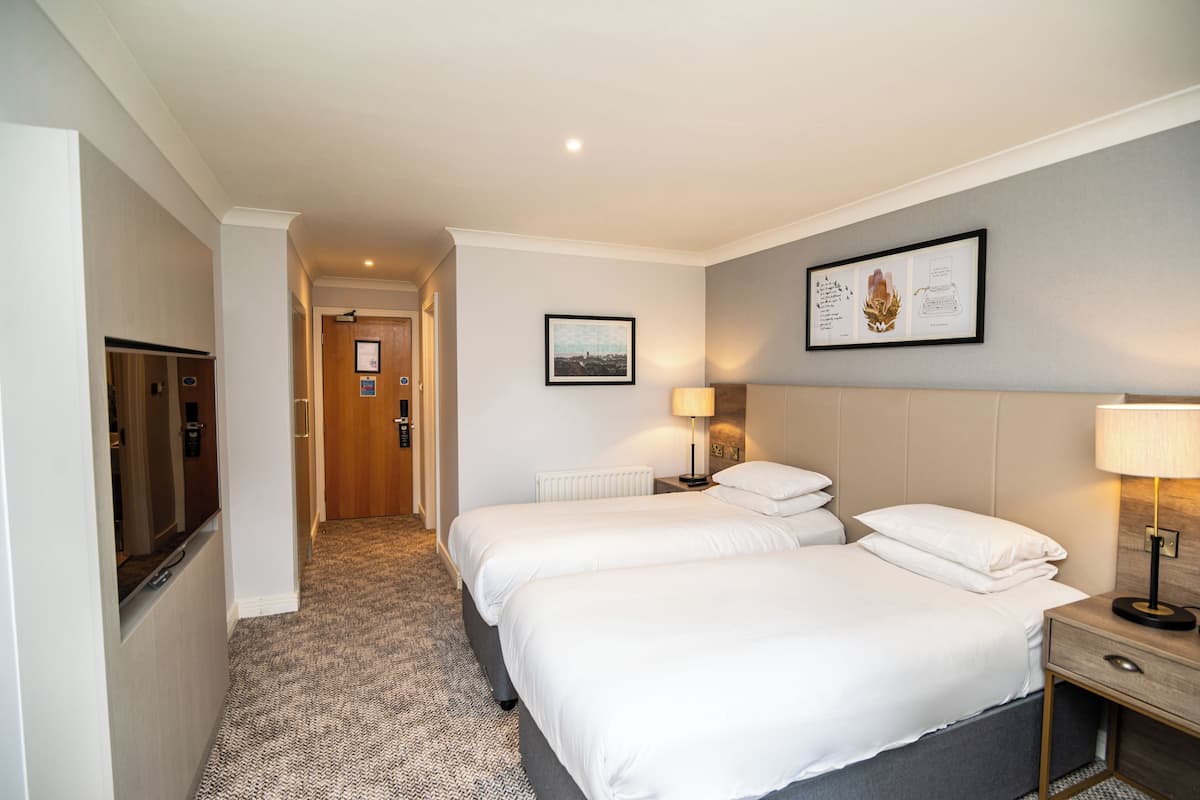 A hotel room with two beds, a wooden door, a radiator, and a framed picture on the wall.