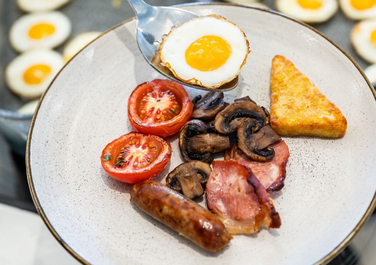 A plate with a fried egg, tomato slices, mushrooms, bacon, and sausage.