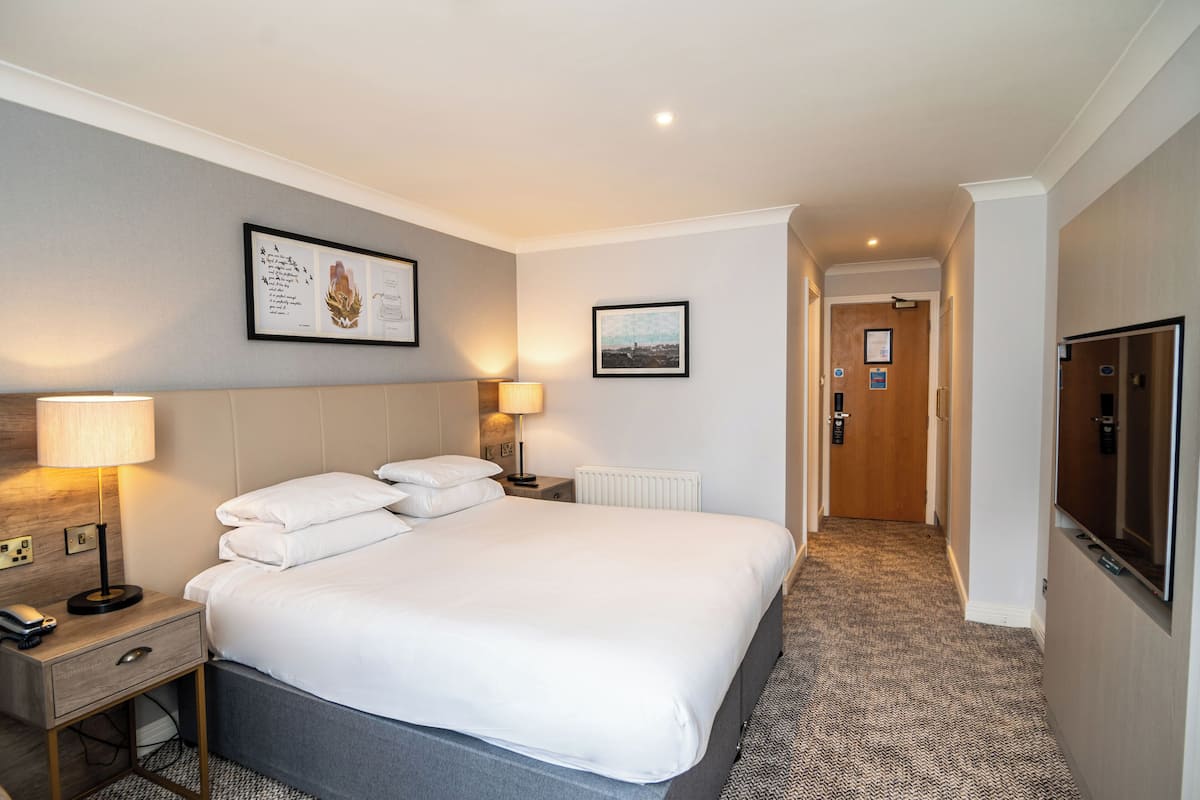 A hotel room with a large bed, two bedside lamps, a framed picture on the wall, and a television on the wall.