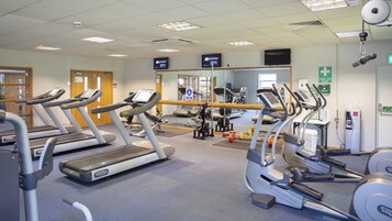 Un gimnasio con cintas de correr, máquinas de pesas y una pared de espejos.