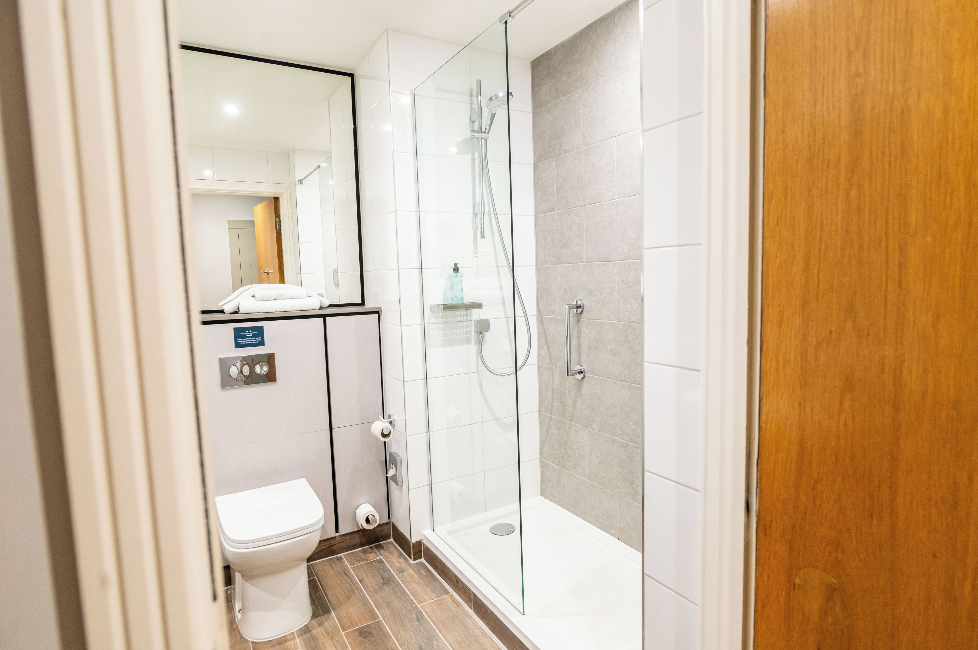 Ein modernes Badezimmer mit einer gläsernen Duschkabine, einer Toilette und einem Spiegel.