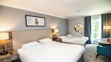 A hotel room with three beds, a desk, a chair, a round mirror, and a framed quote on the wall.