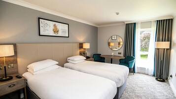 A hotel room with two beds, a desk, a chair, a round mirror, and a window with curtains.