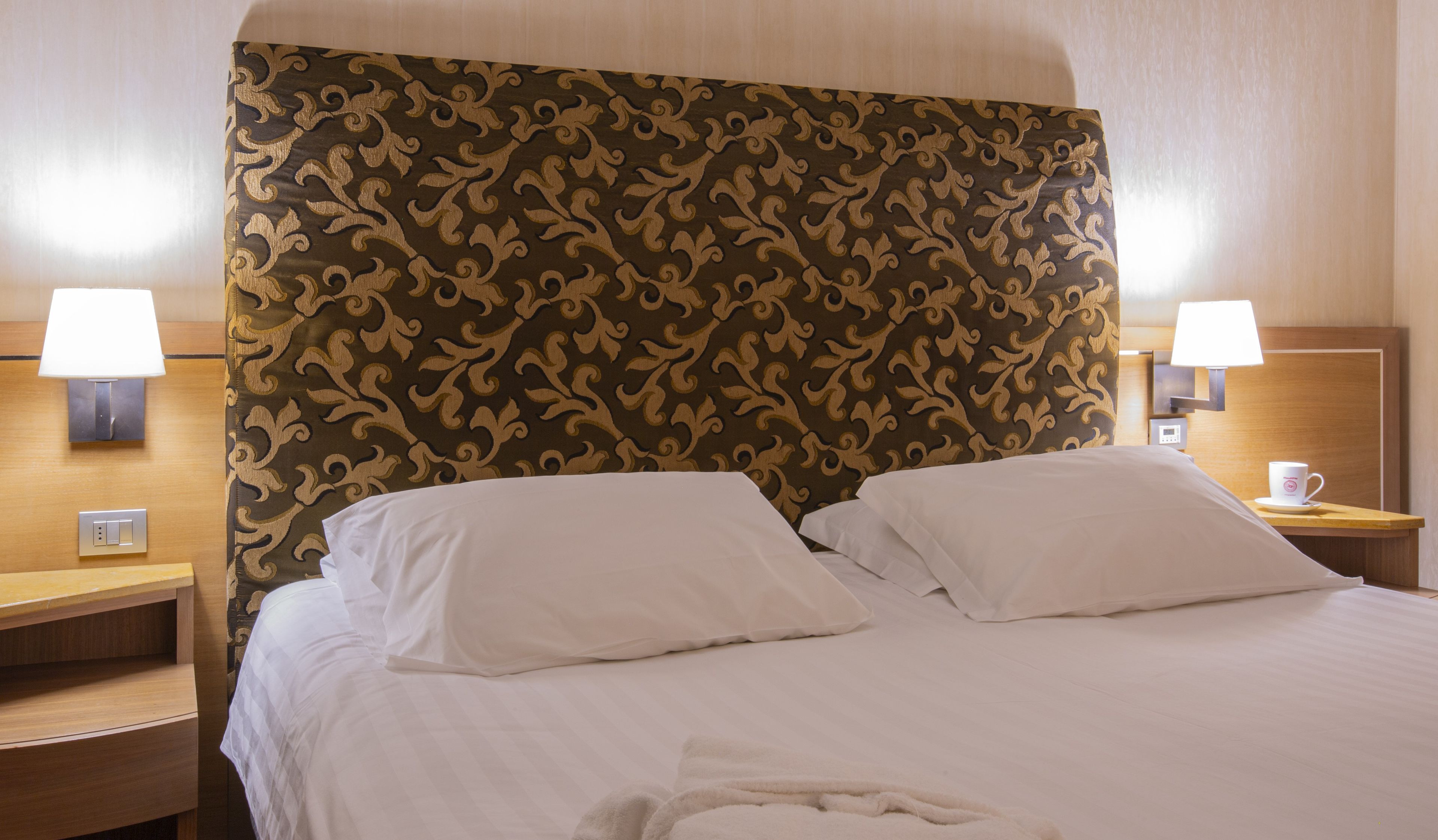 Habitación de hotel con una cama grande, dos lámparas de noche, una mesita de noche y una lámpara de pared.