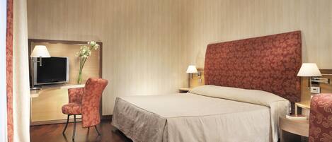 A hotel room with a large bed, two bedside tables with lamps, a TV, a chair, and a desk with a vase of flowers.