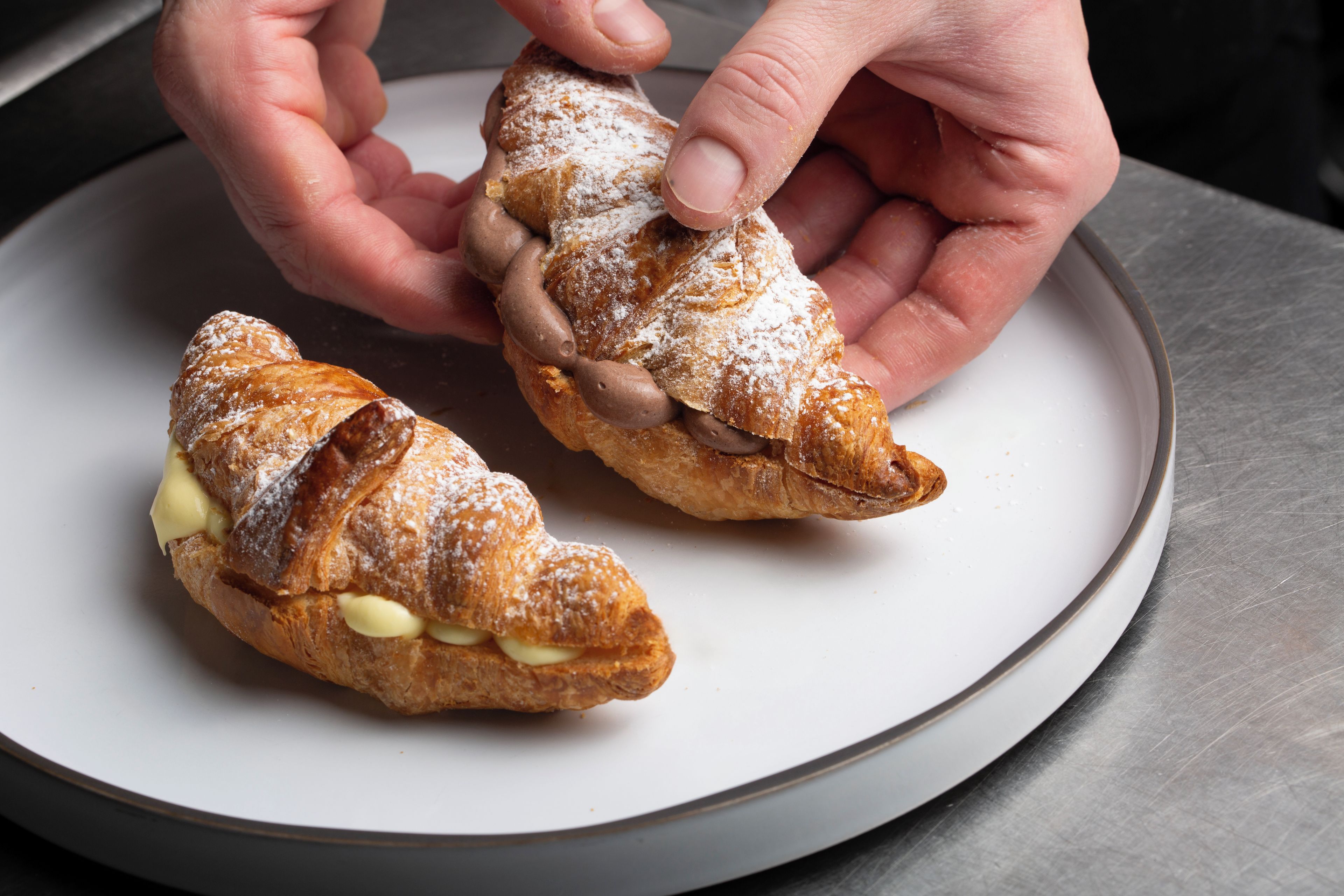 Une assiette avec deux pâtisseries : l’une fourrée à la crème et l’autre au chocolat, toutes deux saupoudrées de sucre glace.