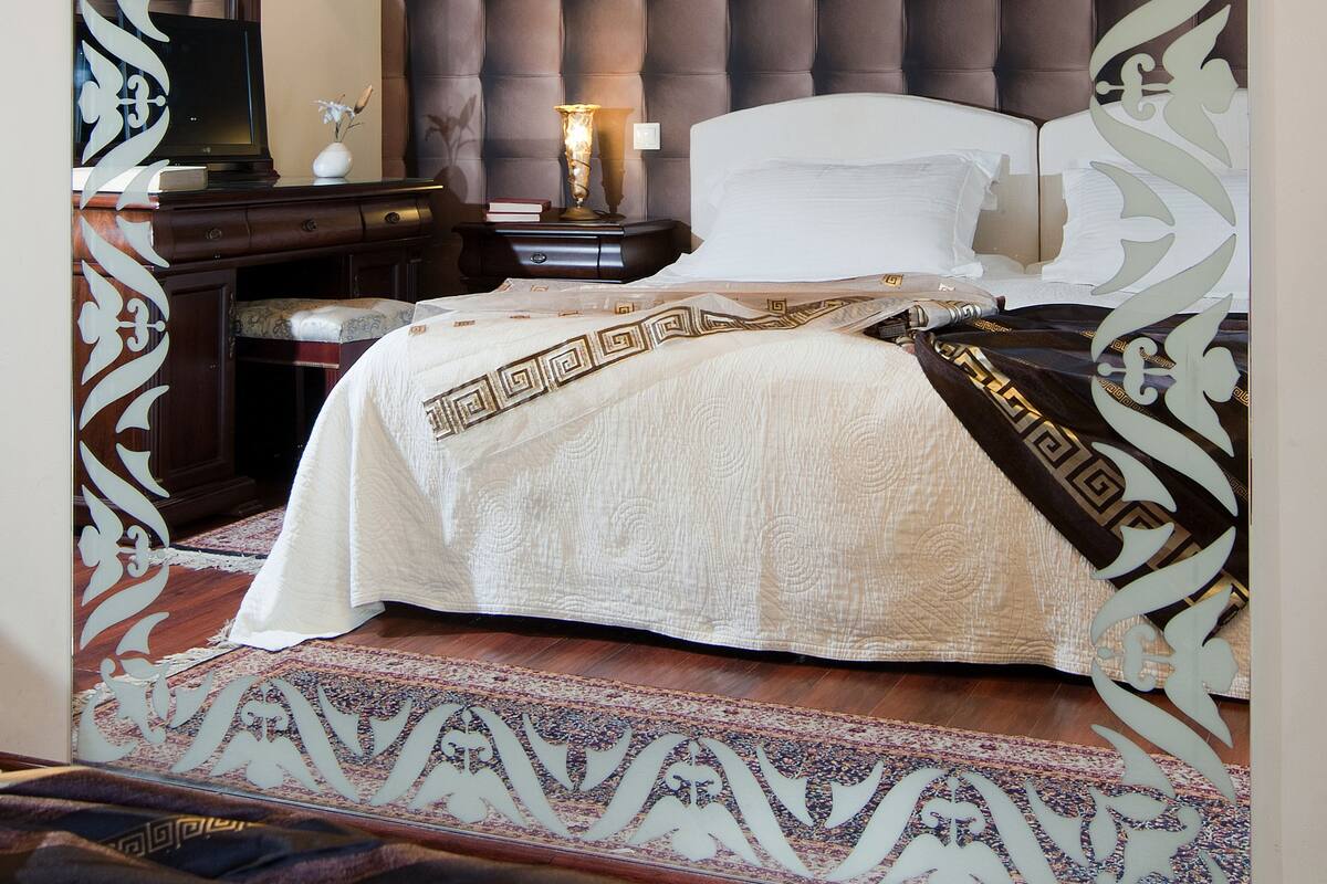 A bedroom with a tufted headboard, a bed with a patterned bedspread, a bedside table with a lamp, and decorative wall art.