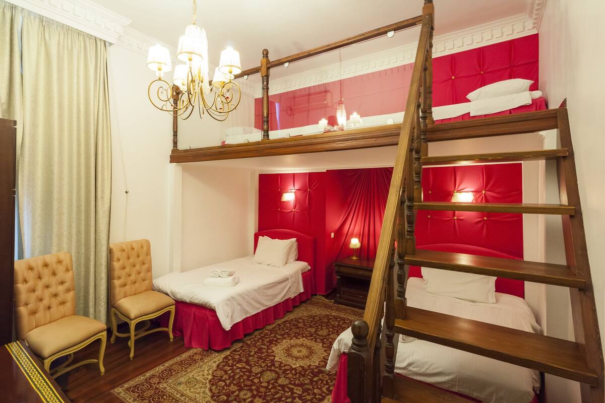 A room with a bunk bed, two chairs, a chandelier, and a red accent wall.