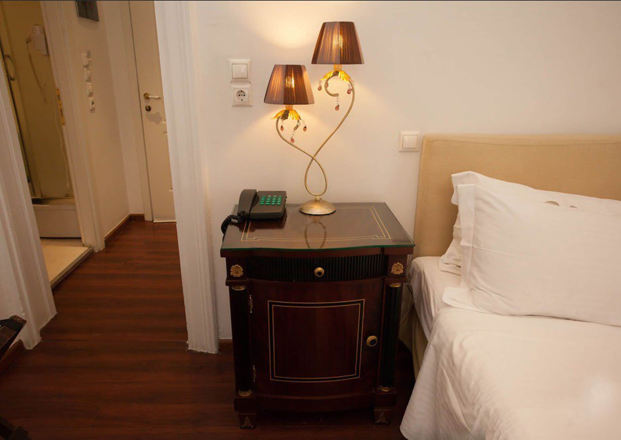 Ein Hotelzimmer mit einem Nachttisch aus Holz, einem Telefon, einer Lampe und einem Bett mit weißer Bettwäsche.