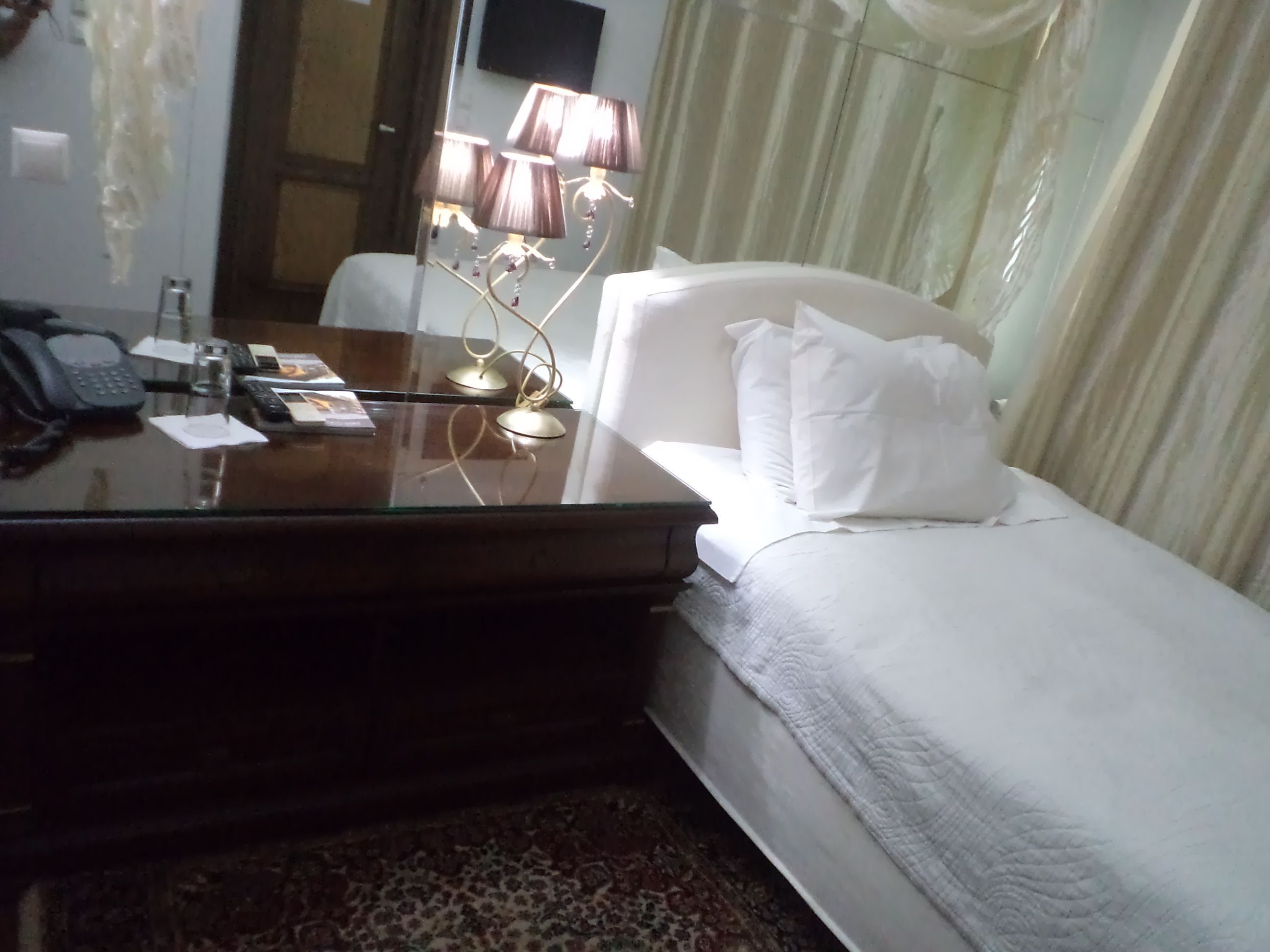 Habitación de hotel con una cama, un escritorio con teléfono, una lámpara y una ventana con cortinas.