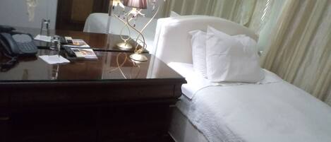 Habitación de hotel con una cama, un escritorio con teléfono, una lámpara y una ventana con cortinas.
