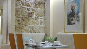 A dining area with a stone wall, a painting, and a table set for two. - Acropolis Museum Boutique Hotel (Athens)