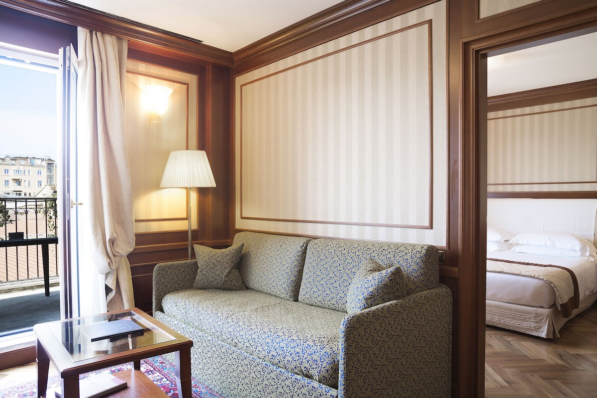 Habitación de hotel con sofá, cama, lámpara y vista a la ciudad desde una ventana.