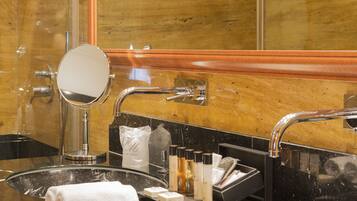 A bathroom with a glass sink, a round mirror, and a vanity area with toiletries.