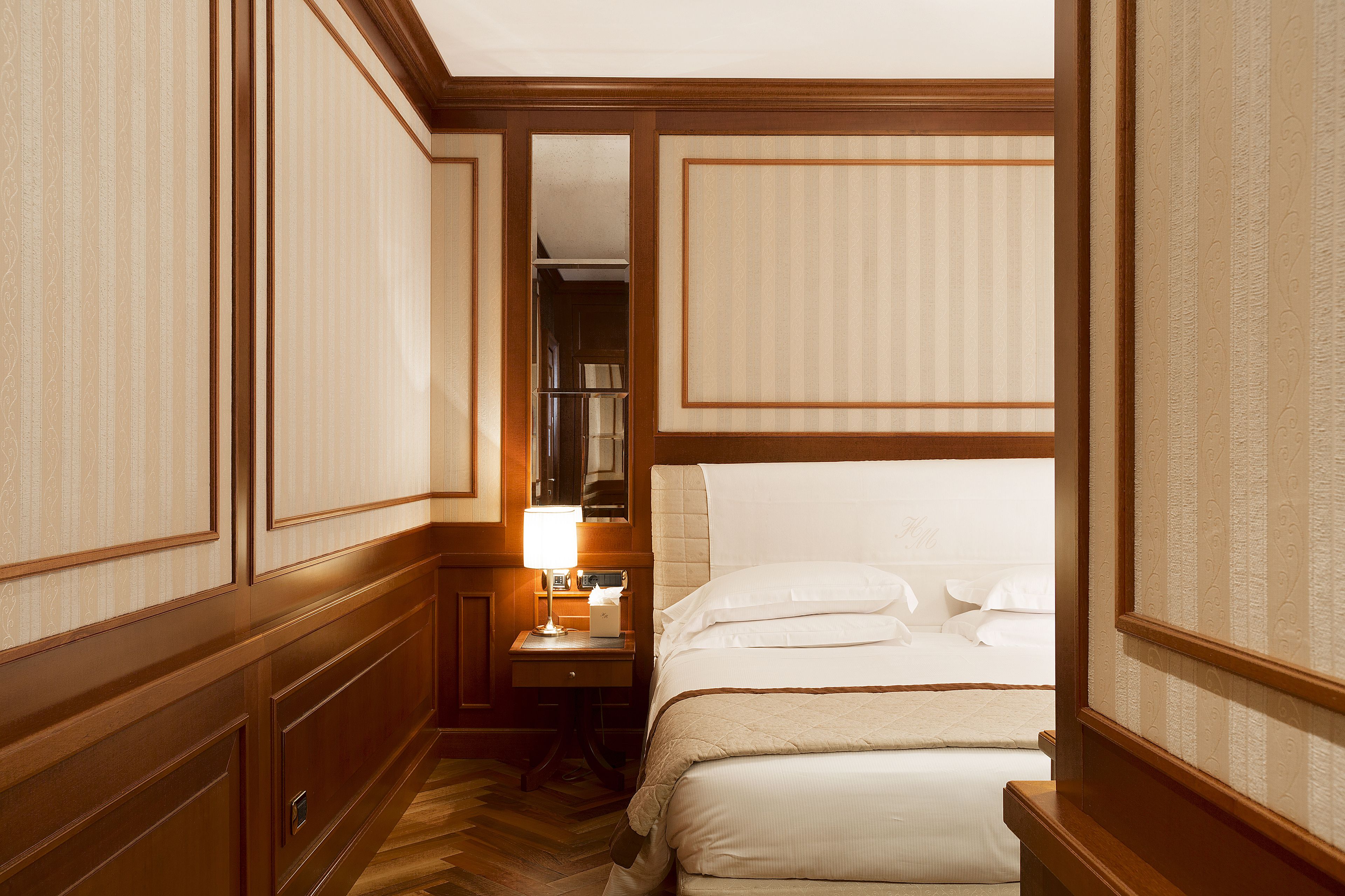 Quarto de hotel com uma cama grande, uma mesa de cabeceira com abajur e um guarda-roupa.
