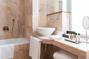 A bathroom with a bathtub, a sink with a large basin, a mirror, and toiletries on the counter.