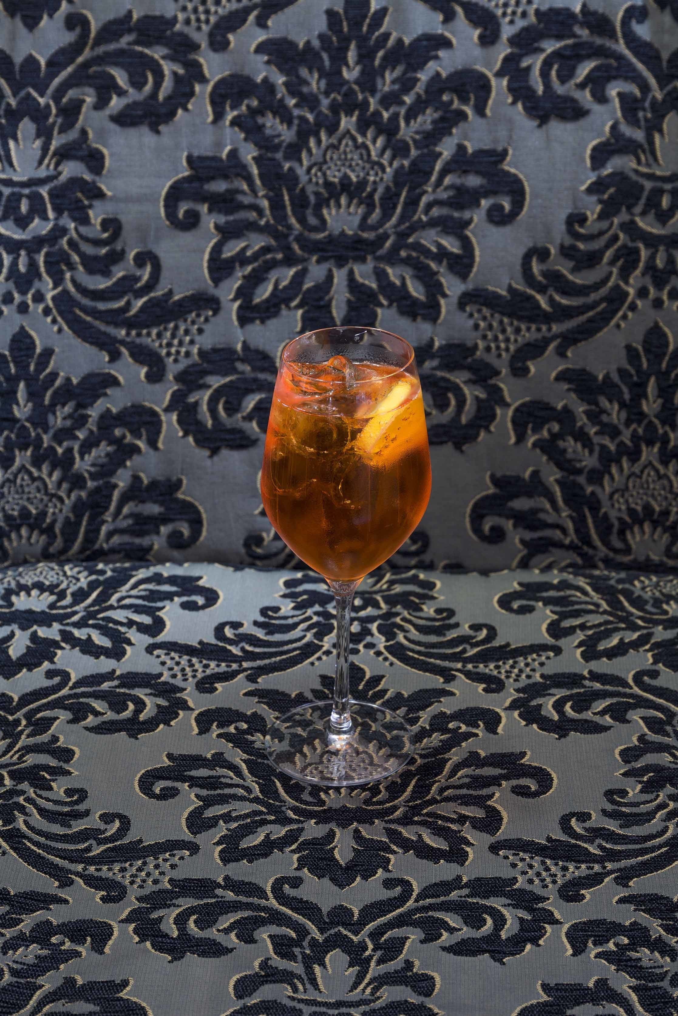 A glass of amber-colored beverage on a patterned fabric surface.