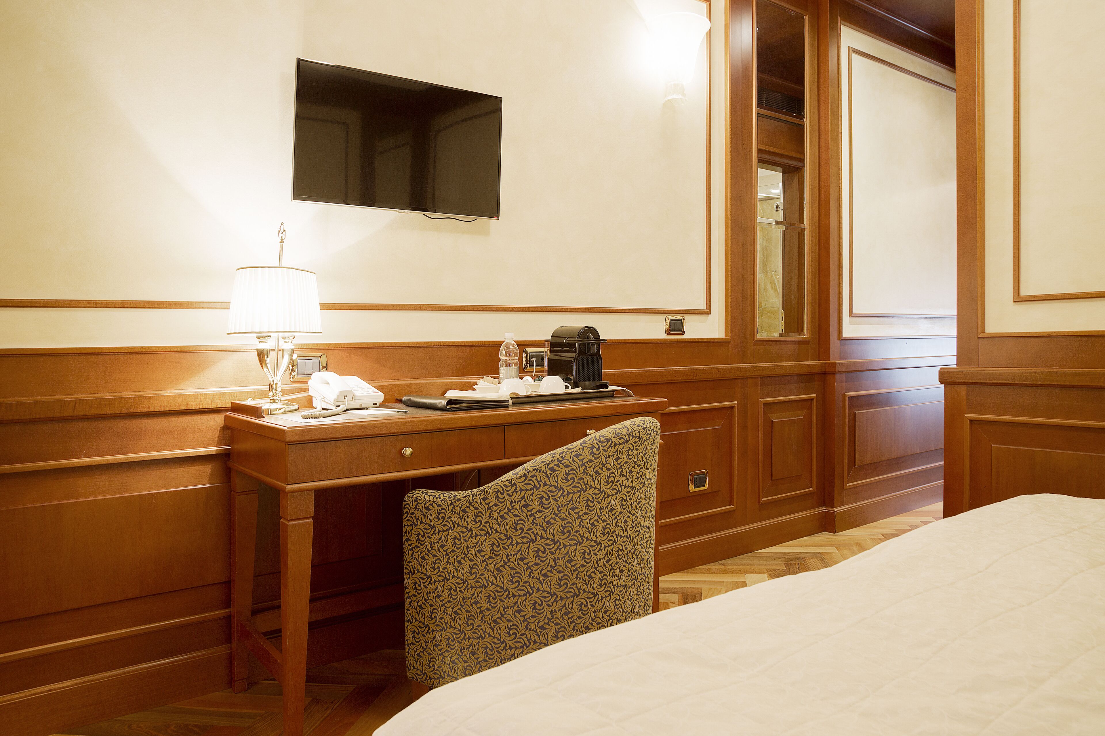Una habitación de hotel con una cama, un escritorio con lámpara, un teléfono y una cafetera.