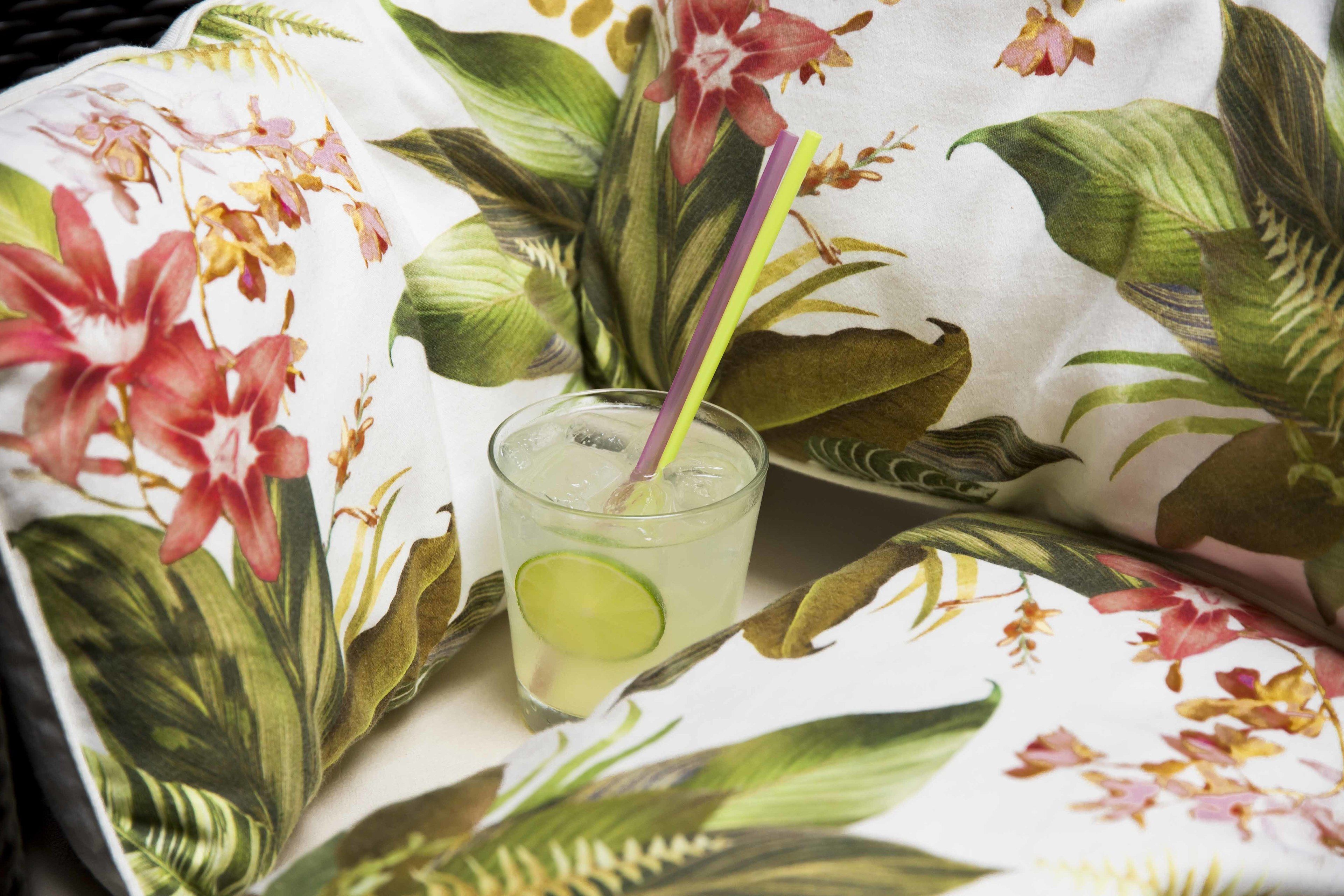 A glass of a clear beverage with a lime slice and a straw, placed on a table with a floral tablecloth.