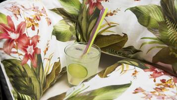 A glass of a clear beverage with a lime slice and a straw, placed on a table with a floral tablecloth.