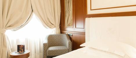 A hotel room with a bed, a bedside table with a book, a chair, and a window with curtains.