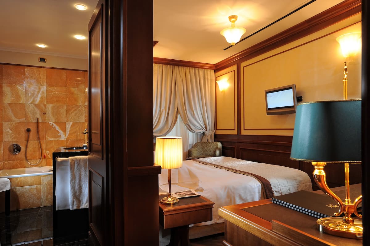 Una habitación de hotel con cama, escritorio, lámpara, televisión y zona de ducha.