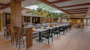 A spacious dining area with high ceilings, exposed wooden beams, and hanging plants.