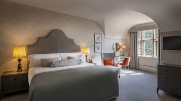 Een hotelkamer met een groot bed, twee bedlampen, een stoel, een televisie en een raam met gordijnen.