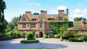 A large, historic building with a symmetrical facade, multiple chimneys, and a well-maintained garden with a circular driveway.