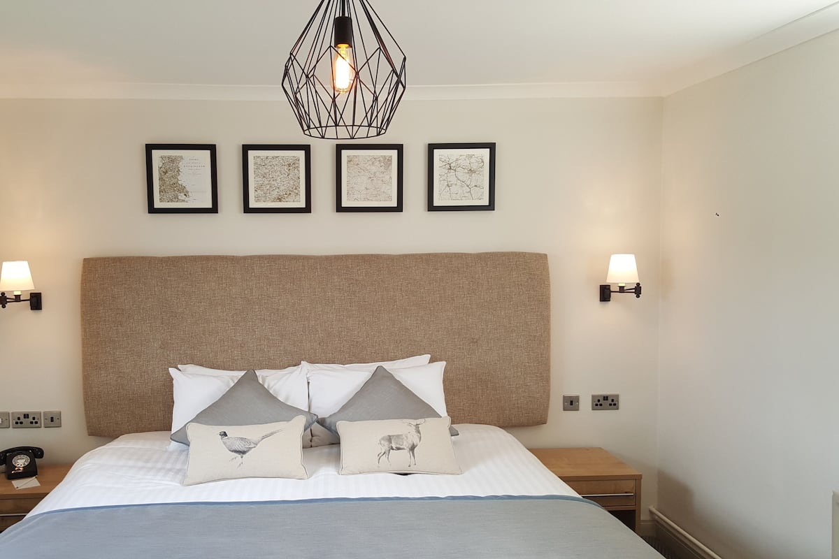 A neatly arranged bedroom with a large bed, a headboard, bedside lamps, and framed artwork on the wall.