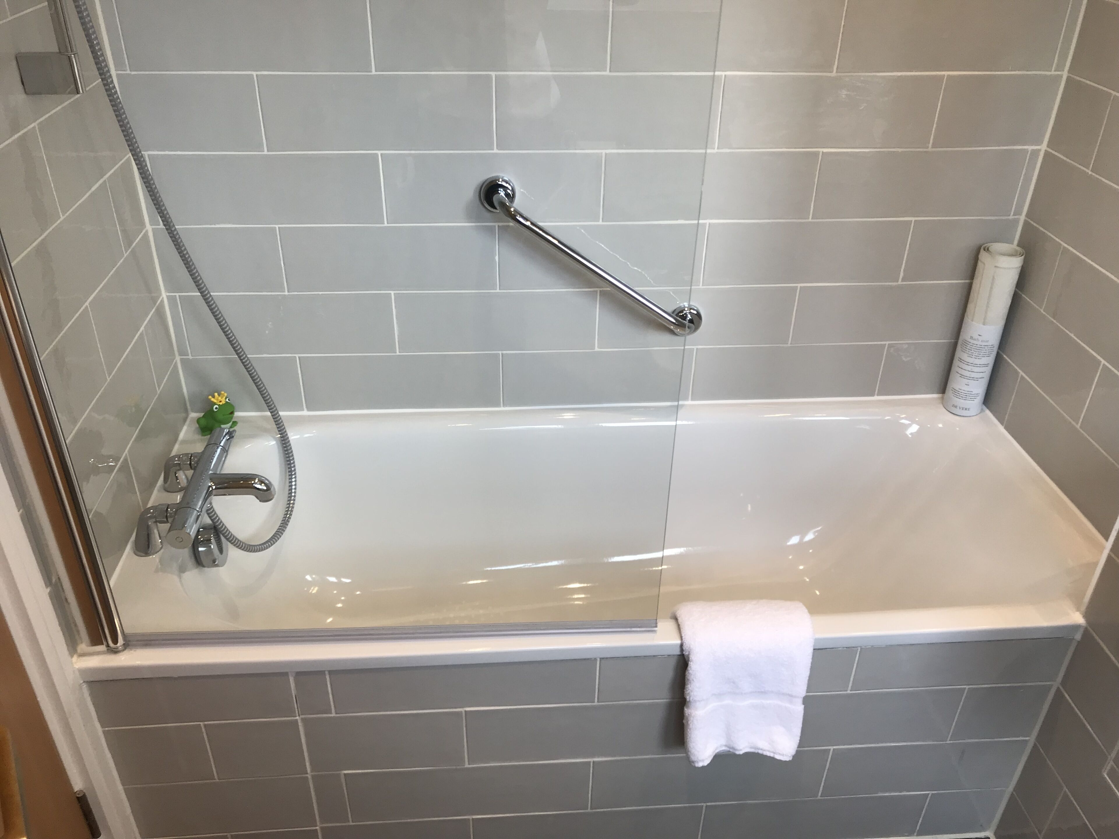 A bathroom with a bathtub, a shower, and a handrail.