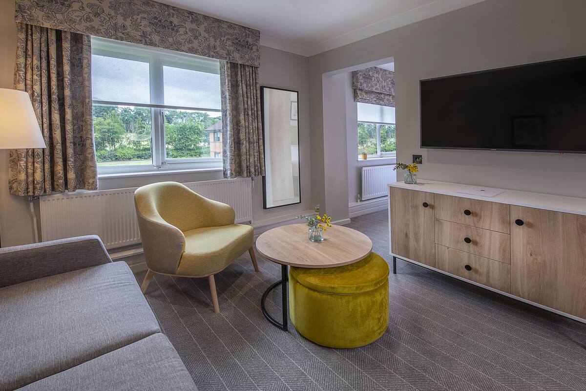 A modern living room with a sofa, armchair, round coffee table, and a TV mounted on the wall.