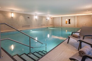 Una piscina interior con superficie de agua cristalina, un juego de escalones que dan acceso a la piscina y una zona de estar con toallas.