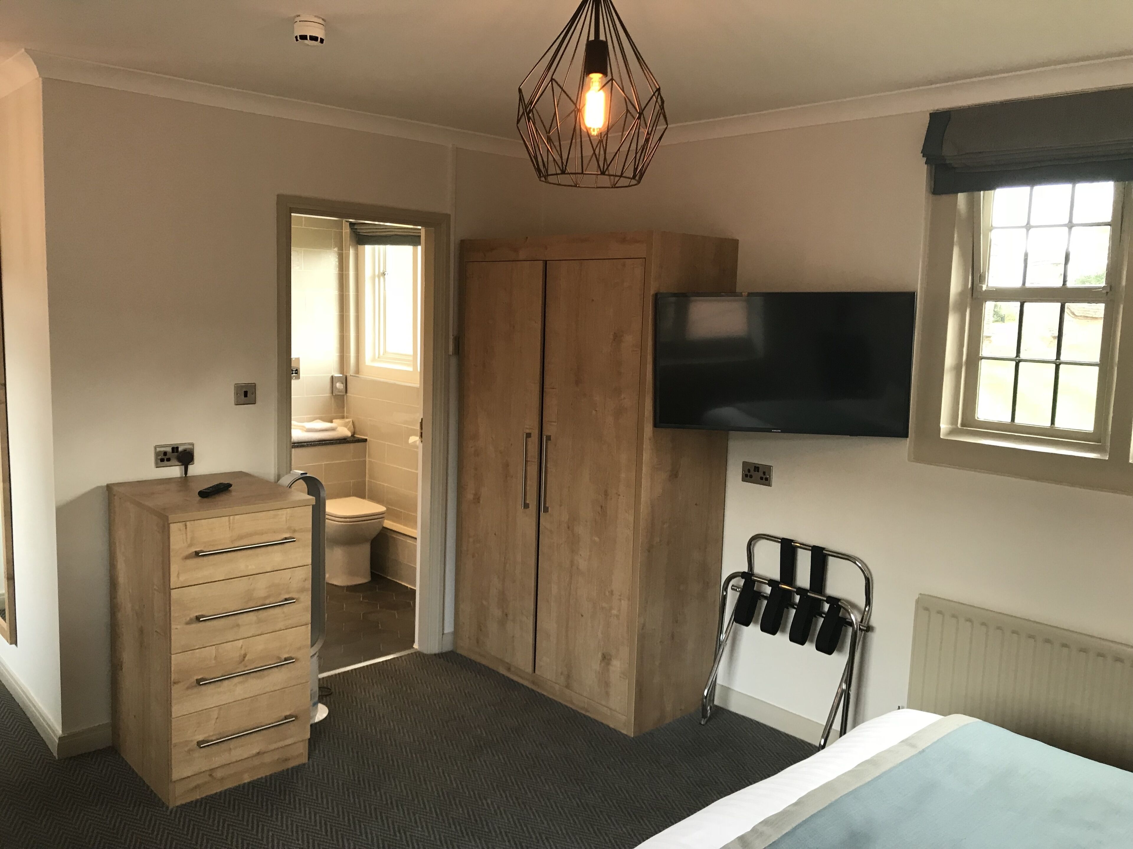 A bedroom with a bed, a wooden wardrobe, a television mounted on the wall, and a window with curtains.