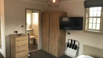A bedroom with a bed, a wooden wardrobe, a television mounted on the wall, and a window with curtains.
