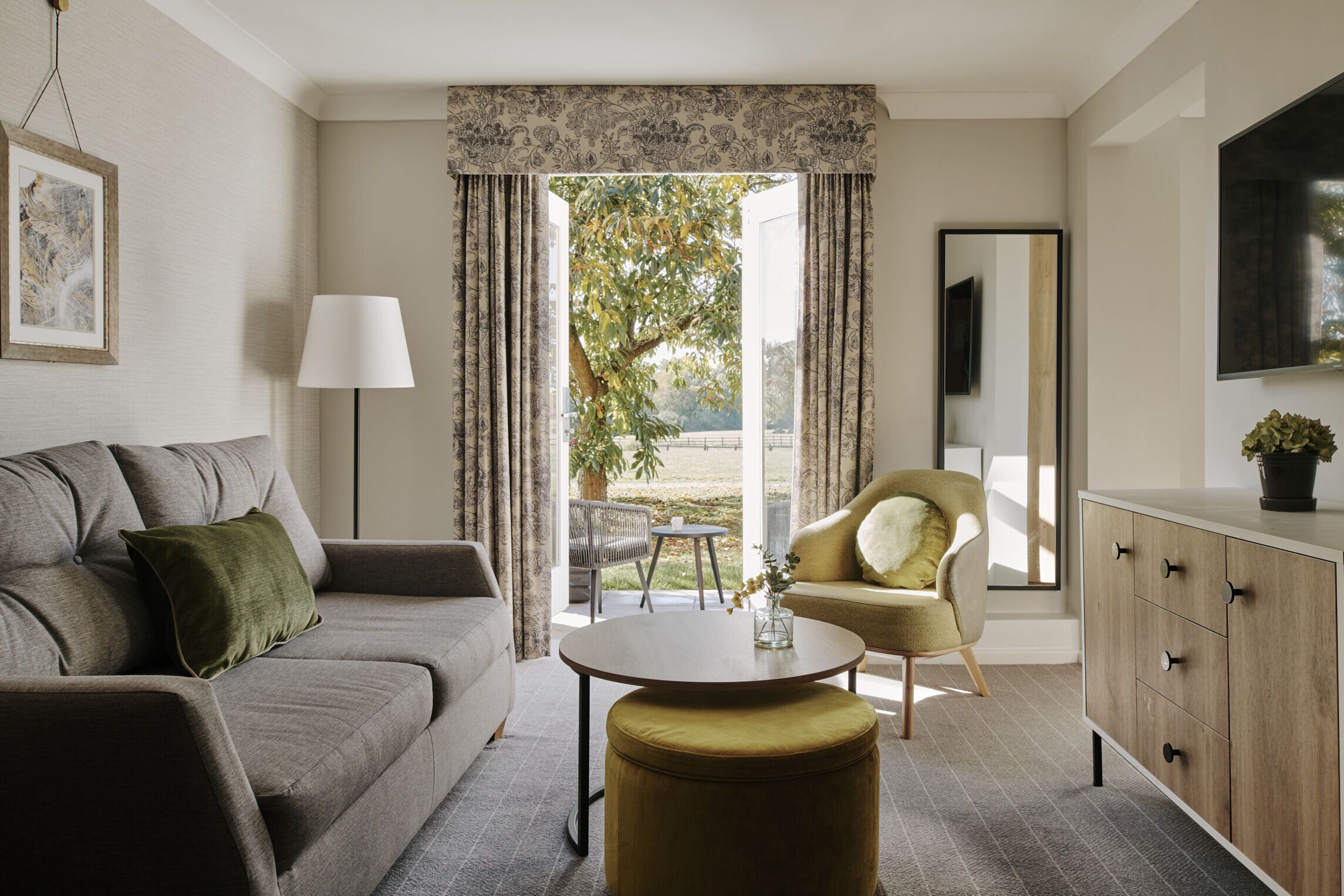 Una sala de estar moderna con un sofá gris, una mesa redonda para café, un sillón amarillo y un mueble con cajones.