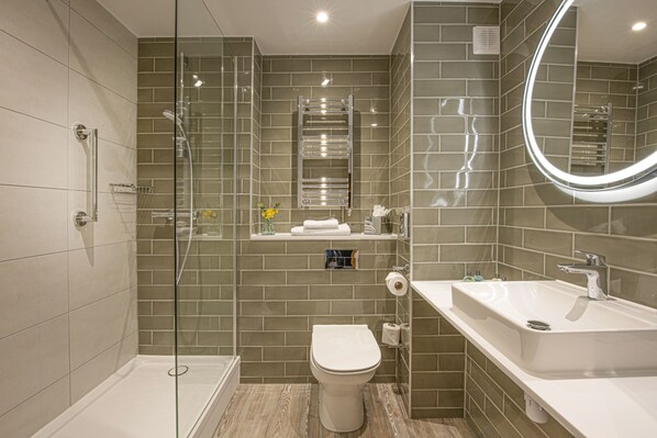 Un baño moderno con cabina de ducha de vidrio, inodoro blanco y una bañera grande independiente.