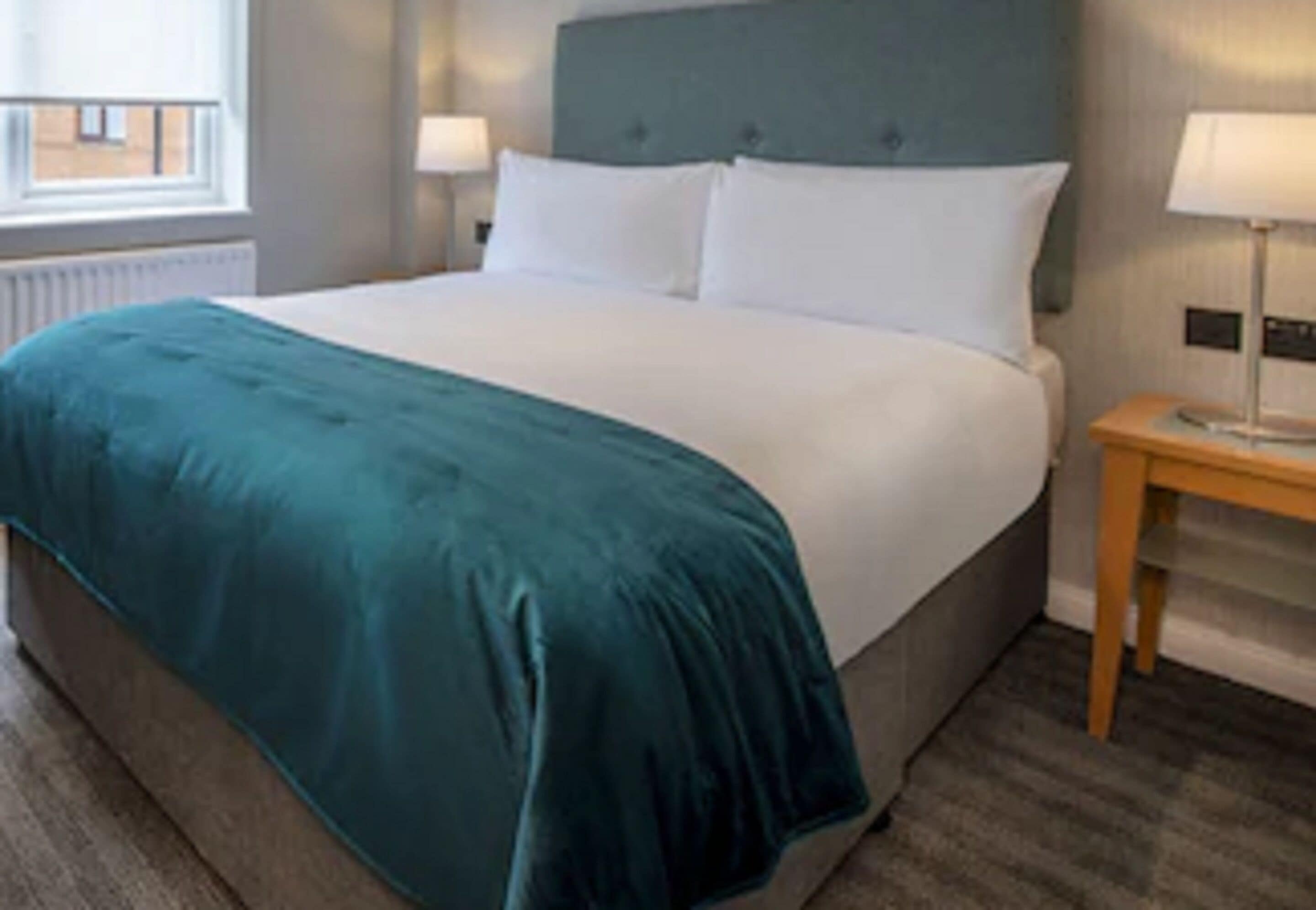 A neatly made bed with a teal bedspread and white pillows in a hotel room.