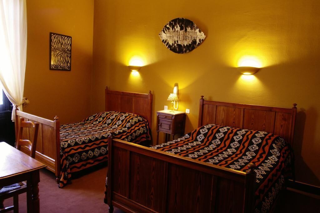 Quarto com duas camas de madeira, uma mesinha e uma mesa de cabeceira com abajur.