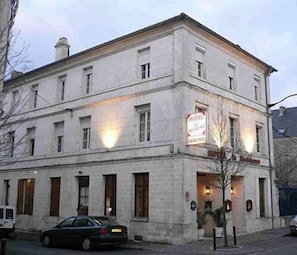 A two-story building with a sign indicating it is a hotel. There are multiple windows on each floor, and the building has a classic architectural style with a flat roof and a chimney. - Arcantis Hotel Heritage (Cognac)