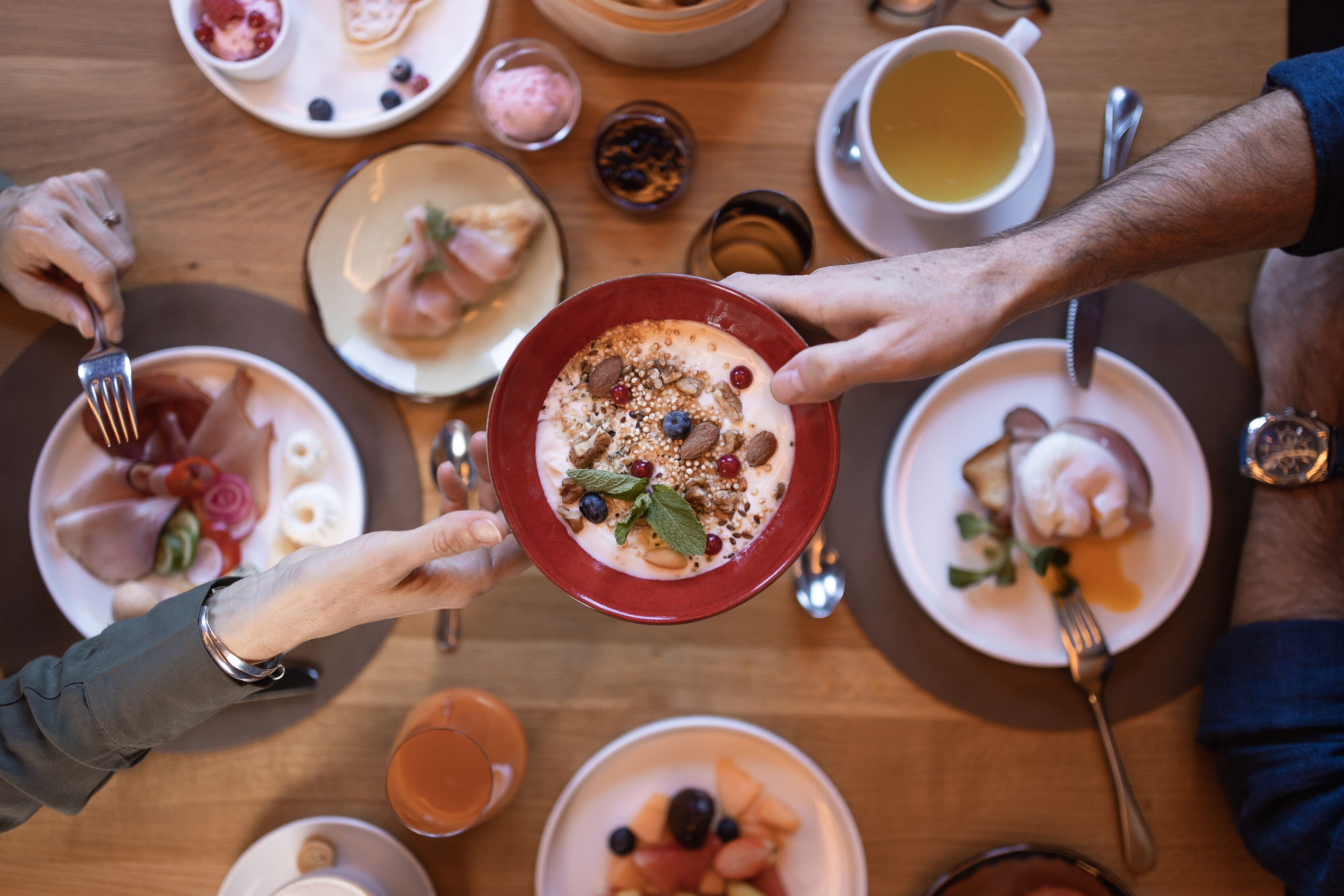 Una mesa de comedor con diversos platos, entre ellos un tazón de yogur con frutas y nueces, y platos con comida y bebidas.