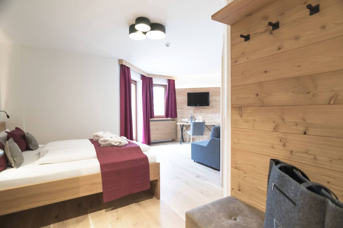 A modern hotel room with a wooden bed, a desk, a chair, and a TV mounted on the wall.