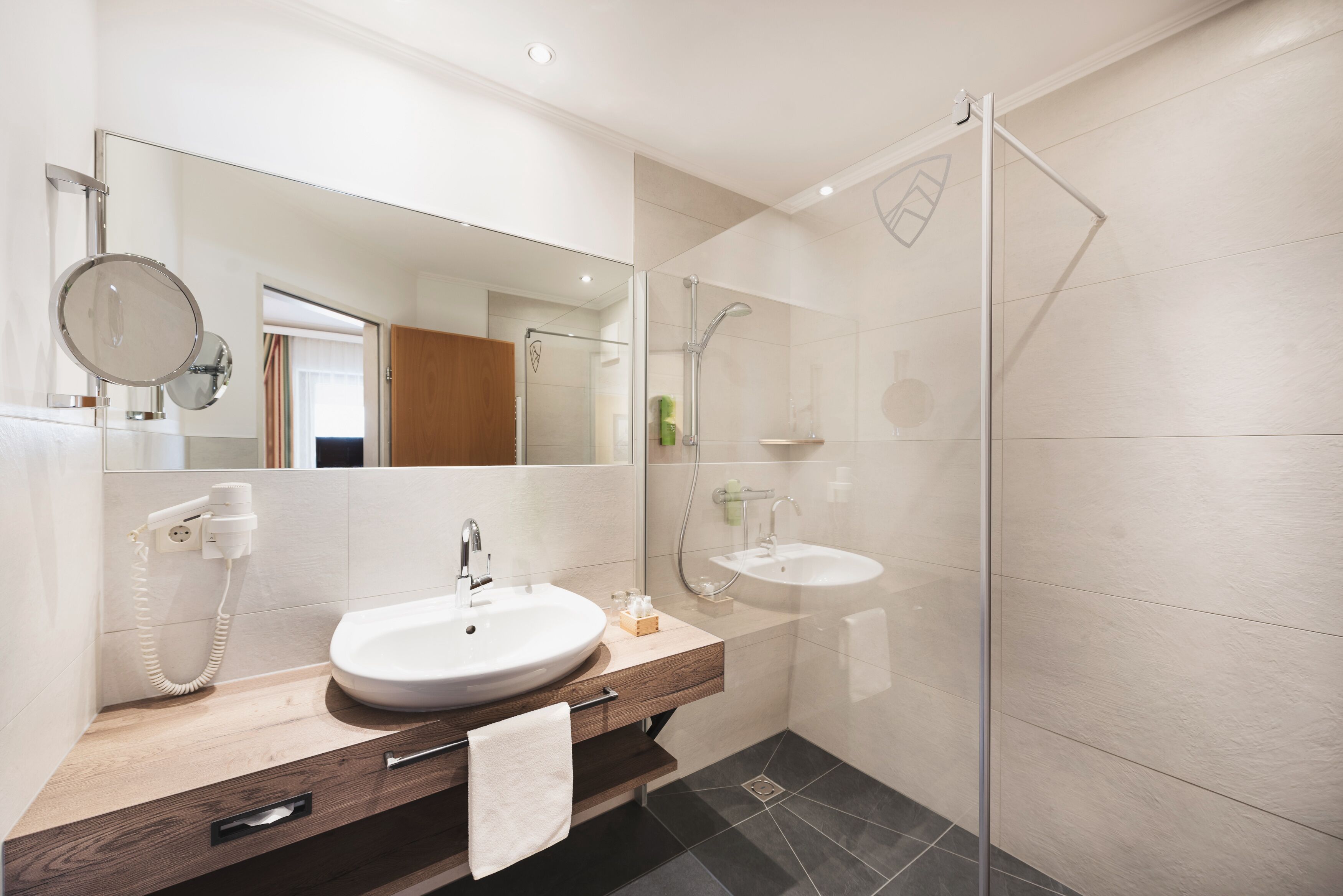 A modern bathroom with a large mirror, two sinks, a shower, and a telephone.