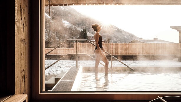 A person in a wooden cabin with a view of a snowy outdoor area and mountains. - Naturhotel Outside (Matrei in Osttirol)